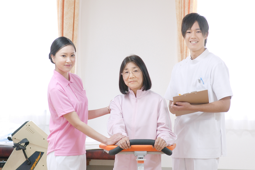 リハビリ室に立つ笑顔の男性看護師と患者と女性理学療法士